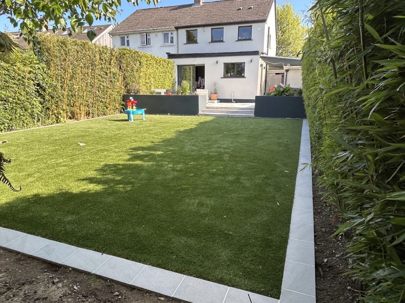 Rectangular artificial lawn with grey porcelain edging behind a rendered Dublin house