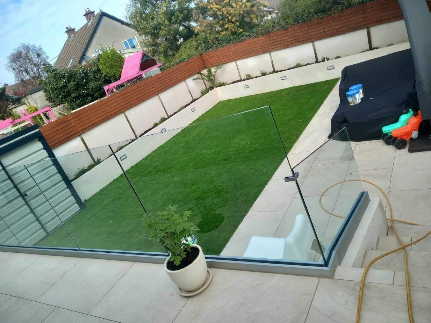Sunken lawn with frameless glass balustrade and porcelain paving in a Dublin back garden