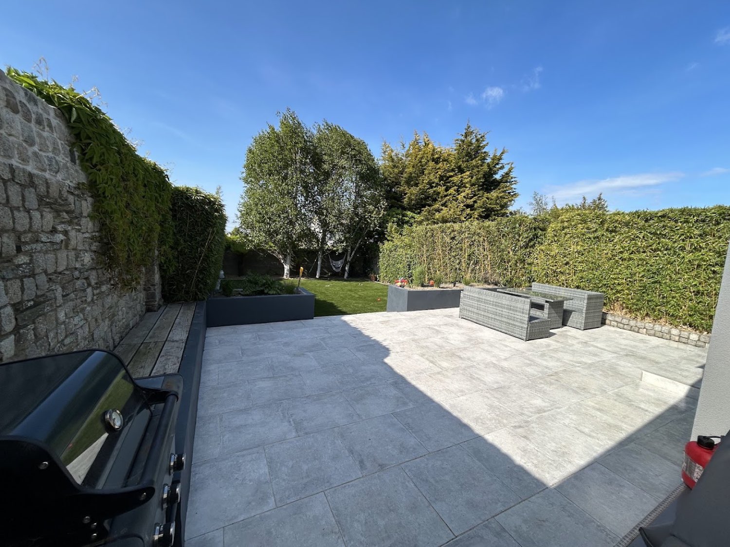 Porcelain-paved garden terrace with rattan seating, clipped hedging and a stone boundary wall, Dublin 6