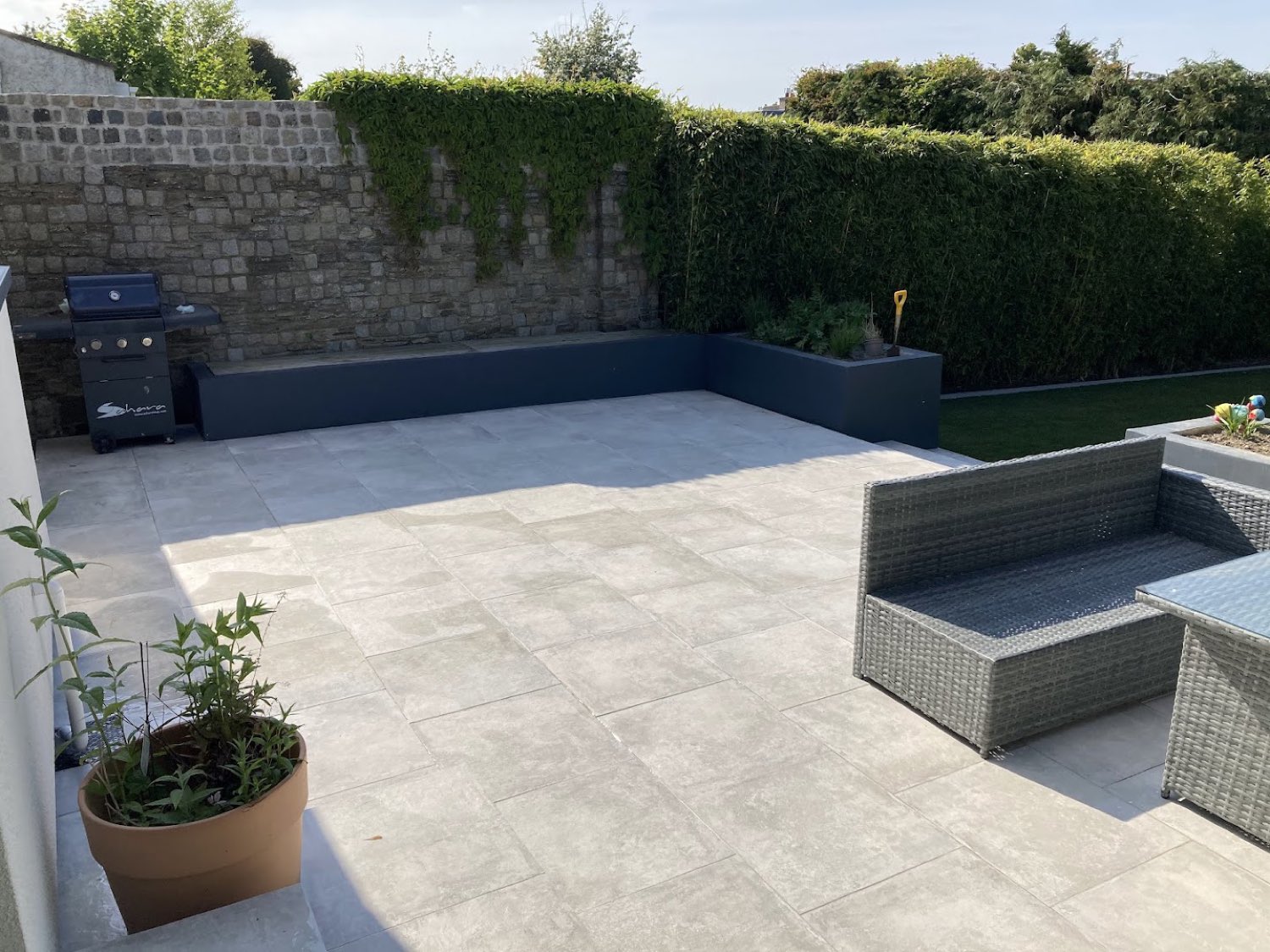 Large porcelain entertaining terrace with rendered raised beds and rattan seating